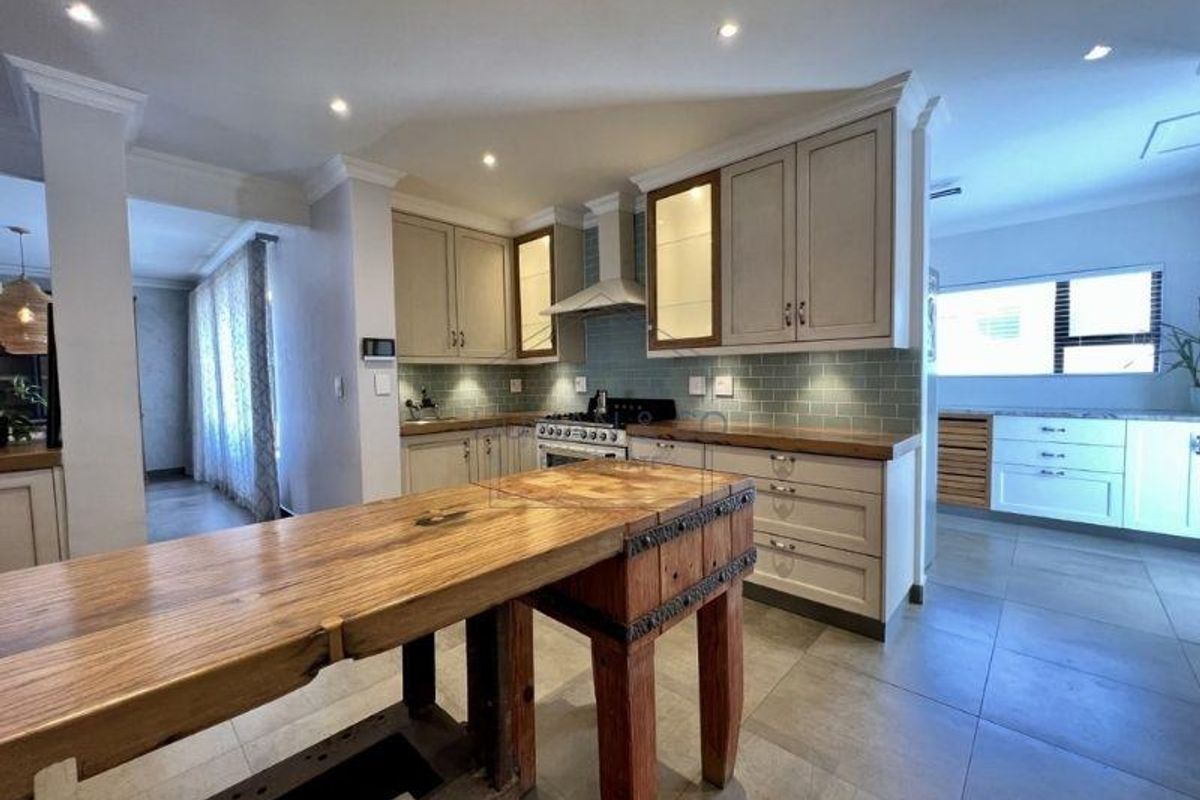 Modern kitchen featuring light-toned cabinetry, subway tile backsplash, wooden countertops, and a central butcher block island with integrated lighting.