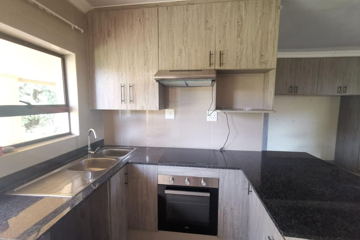 A functional kitchen featuring modern wood-look cabinetry, granite countertops, a built-in oven, electric hob, and a stainless steel double sink.