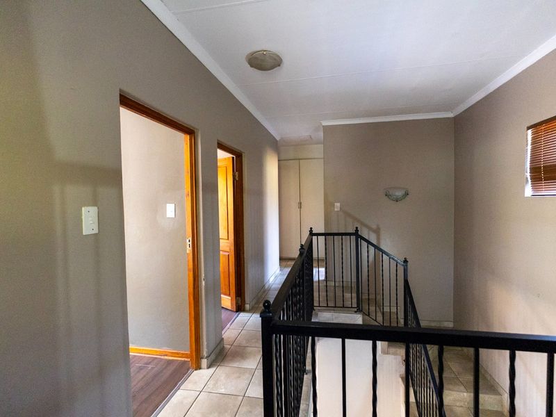 A spacious upper-level hallway featuring tiled flooring, a decorative wrought iron balustrade, and built-in storage cupboards.
