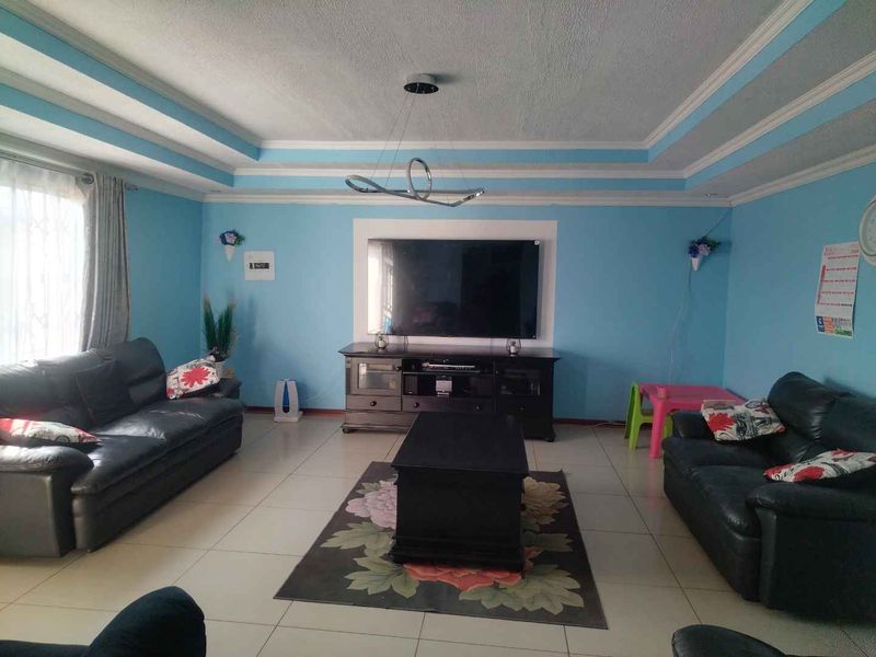Spacious living room featuring a decorative tray ceiling, tiled flooring, and a central wall-mounted television area.