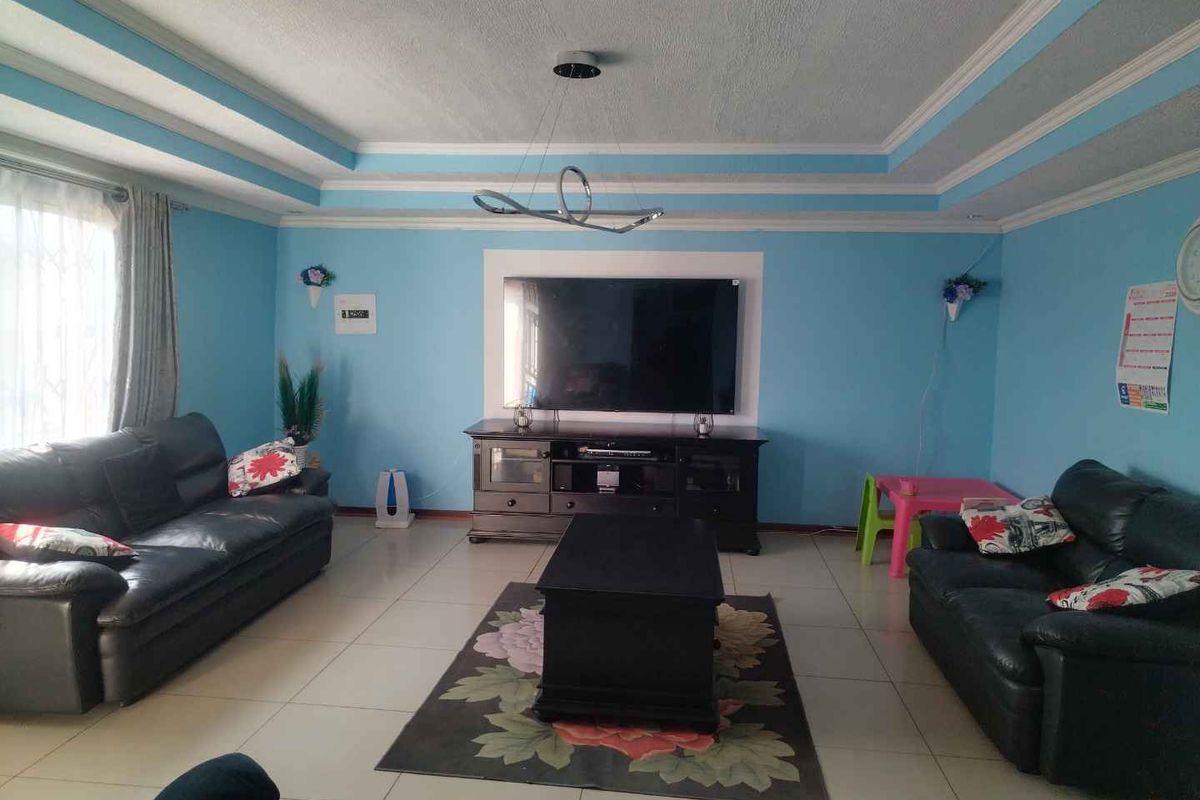 Spacious living room featuring a decorative tray ceiling, tiled flooring, and a central wall-mounted television area.