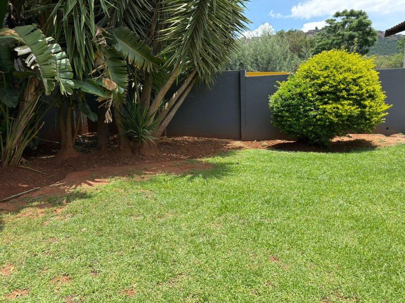 A well-maintained private garden area featuring a manicured lawn, mature landscaping, and a secure perimeter wall with electric fencing.