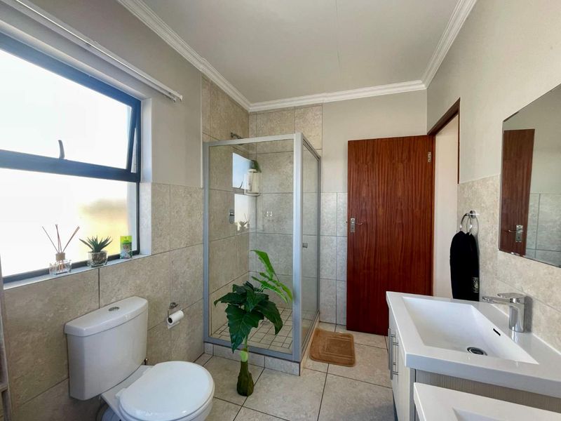 A well-maintained bathroom featuring a glass shower enclosure, modern vanity with basin, neutral wall and floor tiling, and a top-hung window.
