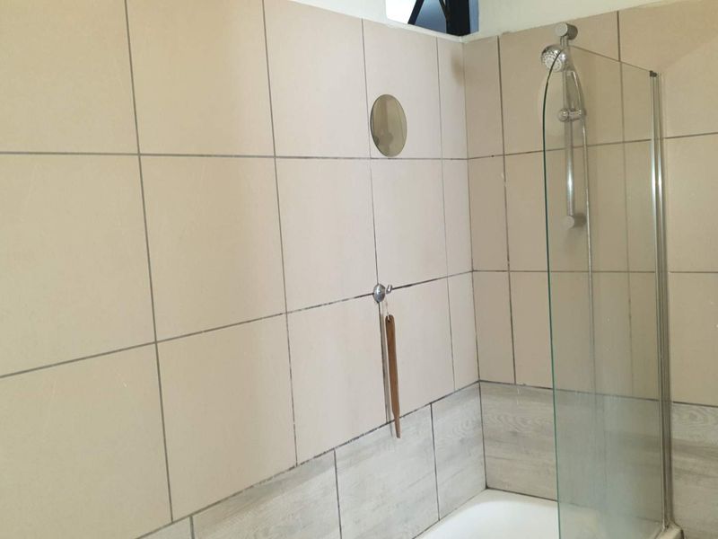 A functional bathroom featuring a bathtub with a glass shower screen and neutral wall tiling.