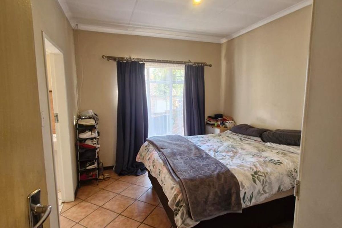 A standard bedroom featuring tiled flooring, a window with curtain rails, and access to an adjacent room.