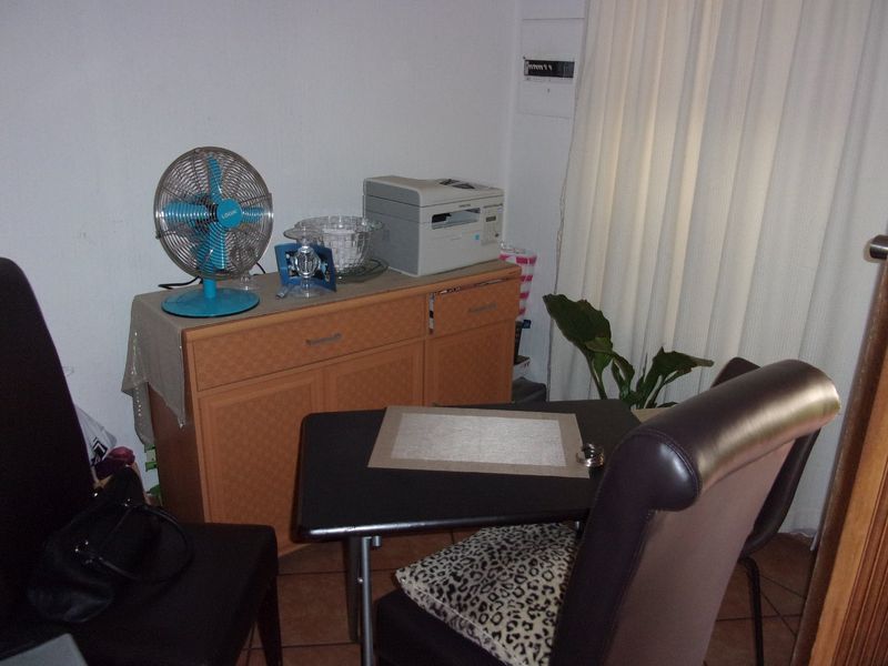 A small room currently utilized as a home office space, featuring tiled flooring and a wall-mounted electrical distribution board.
