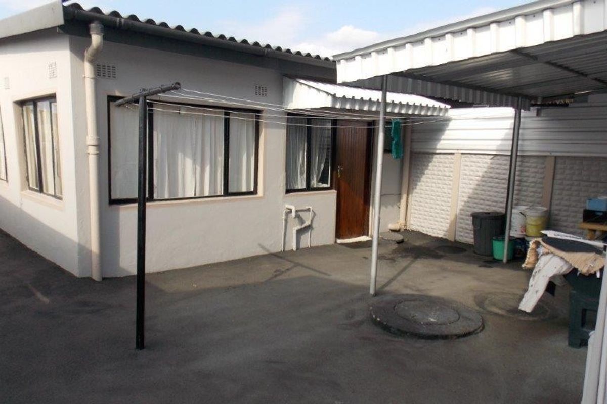Rear exterior area featuring asphalt paving, a metal carport structure, and a precast concrete boundary wall.
