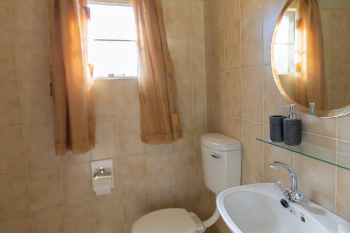 A functional bathroom featuring neutral ceramic wall and floor tiles, a pedestal washbasin with chrome mixer, and a standard toilet.