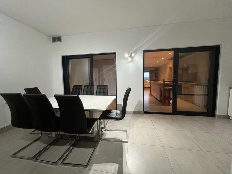 Open plan dining area featuring large sliding glass doors that provide a view into the adjacent kitchen space and modern tiled flooring throughout.