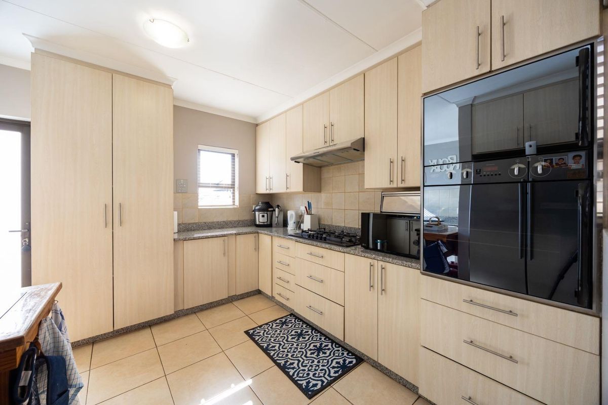 A functional kitchen featuring light wood-finish cabinetry, granite countertops, a gas hob with extractor, and a built-in oven, complemented by neutral tiled flooring.