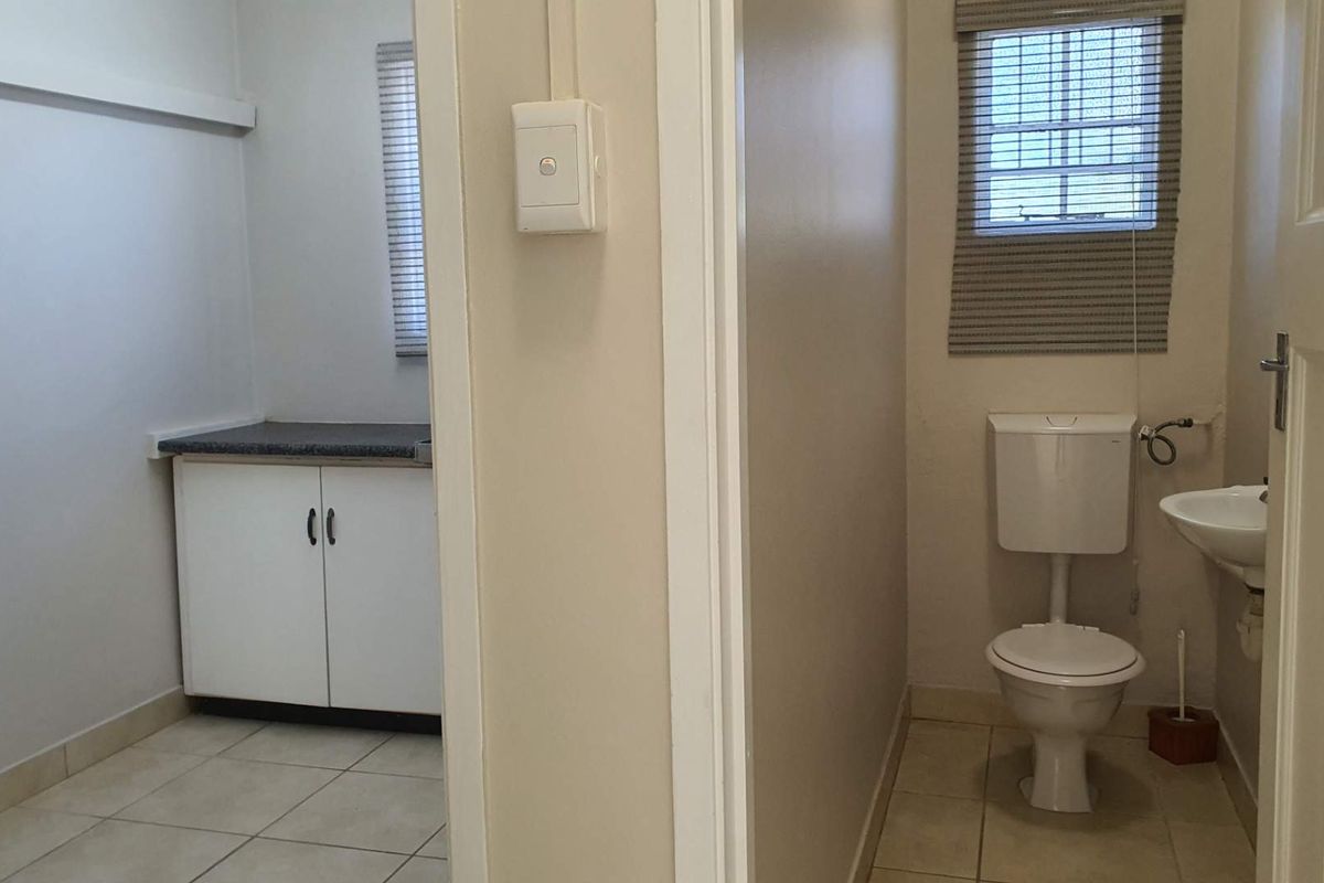 A functional office bathroom and adjacent utility area featuring tiled flooring, a standard toilet, wall-mounted basin, and built-in storage cabinetry.