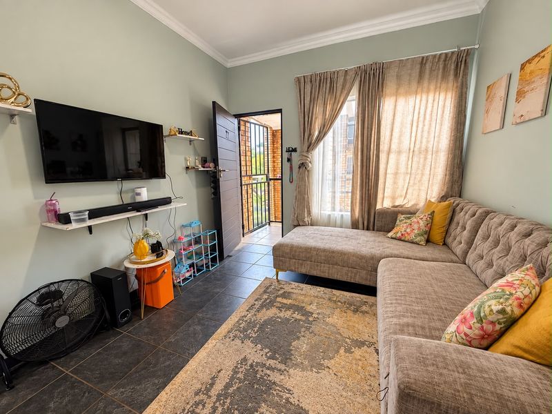 A cozy living room featuring tiled flooring, crown molding, and direct access to an outdoor balcony area through a secure entrance door.