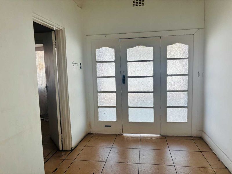 An empty entrance hall featuring tiled flooring and a classic multi-pane glass panel door, providing a blank canvas for renovation.