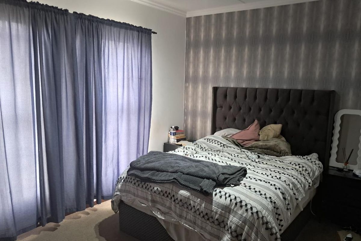 A bedroom featuring a patterned accent wall, neutral carpeting, and window treatments.