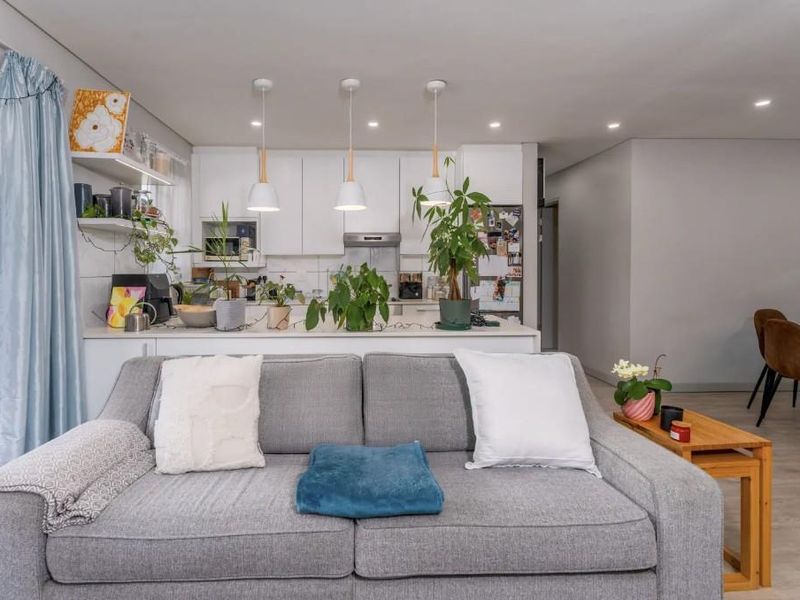 An open-plan living and kitchen area featuring modern cabinetry, pendant lighting, and seamless flow to an outdoor balcony through sliding glass doors.
