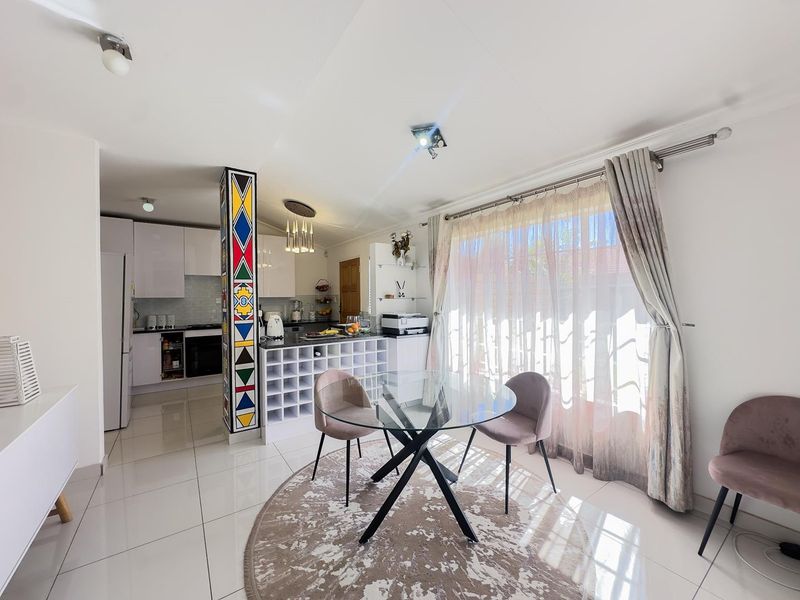 An open-plan kitchen and dining area featuring modern white cabinetry, a decorative pillar, tiled flooring, and a functional kitchen island with built-in wine storage.