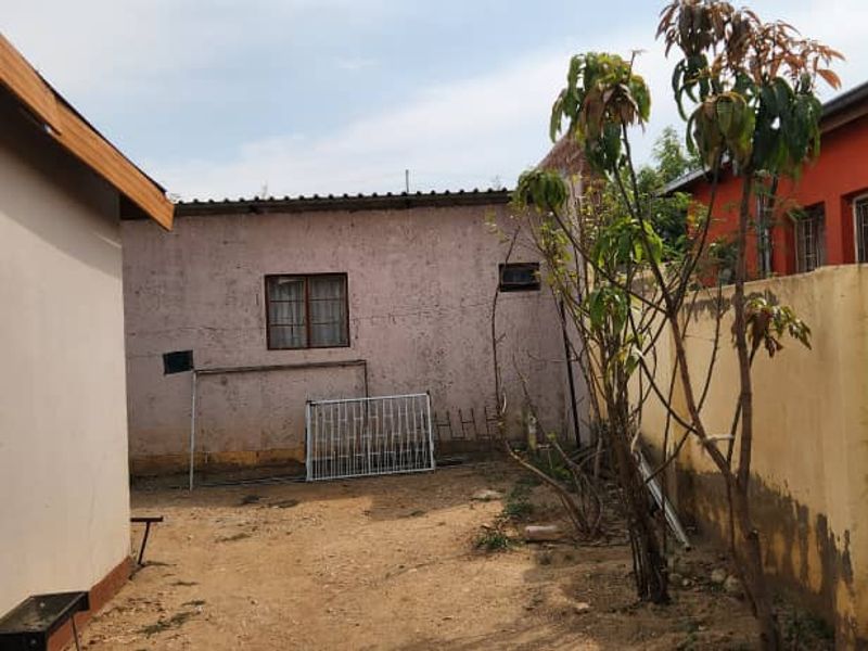 A rear exterior view of the property showing a small yard area, perimeter boundary walls, and the rear facade of the building.