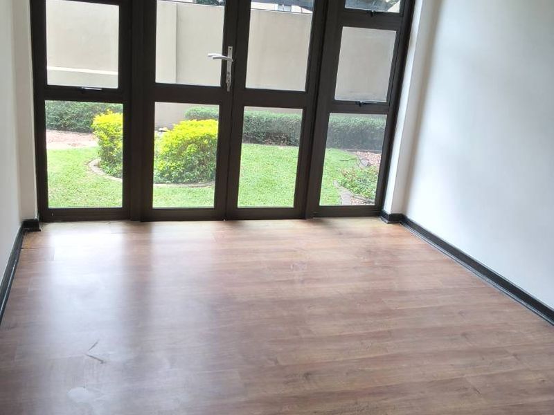 An empty living room featuring laminate flooring and large aluminium-framed glass doors providing natural light and garden views.