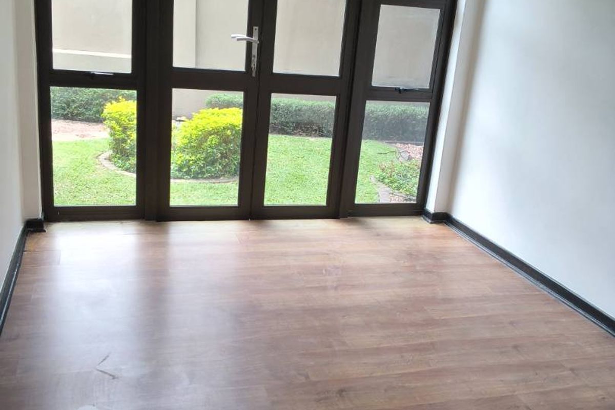 An empty living room featuring laminate flooring and large aluminium-framed glass doors providing natural light and garden views.