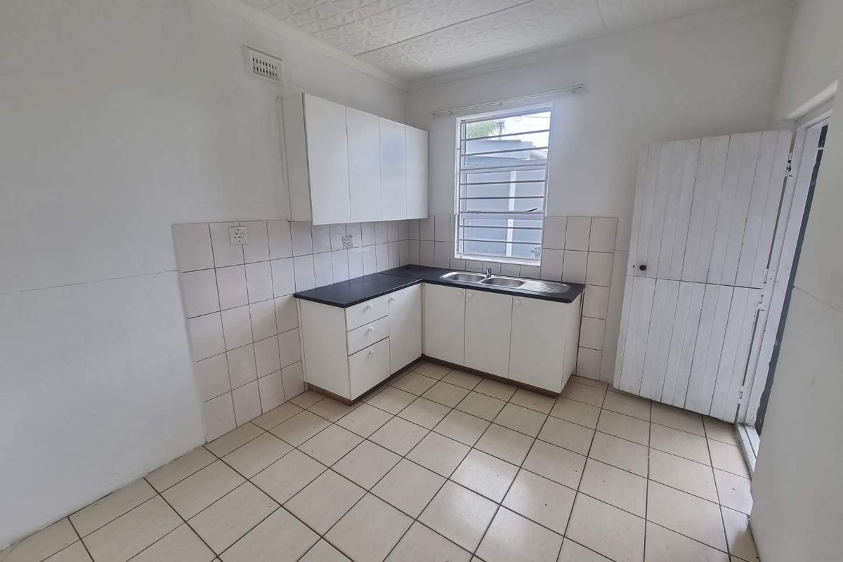 A functional, empty kitchen featuring white built-in cabinetry, a stainless steel sink, tiled backsplash, and neutral floor tiles, ready for a modern update.