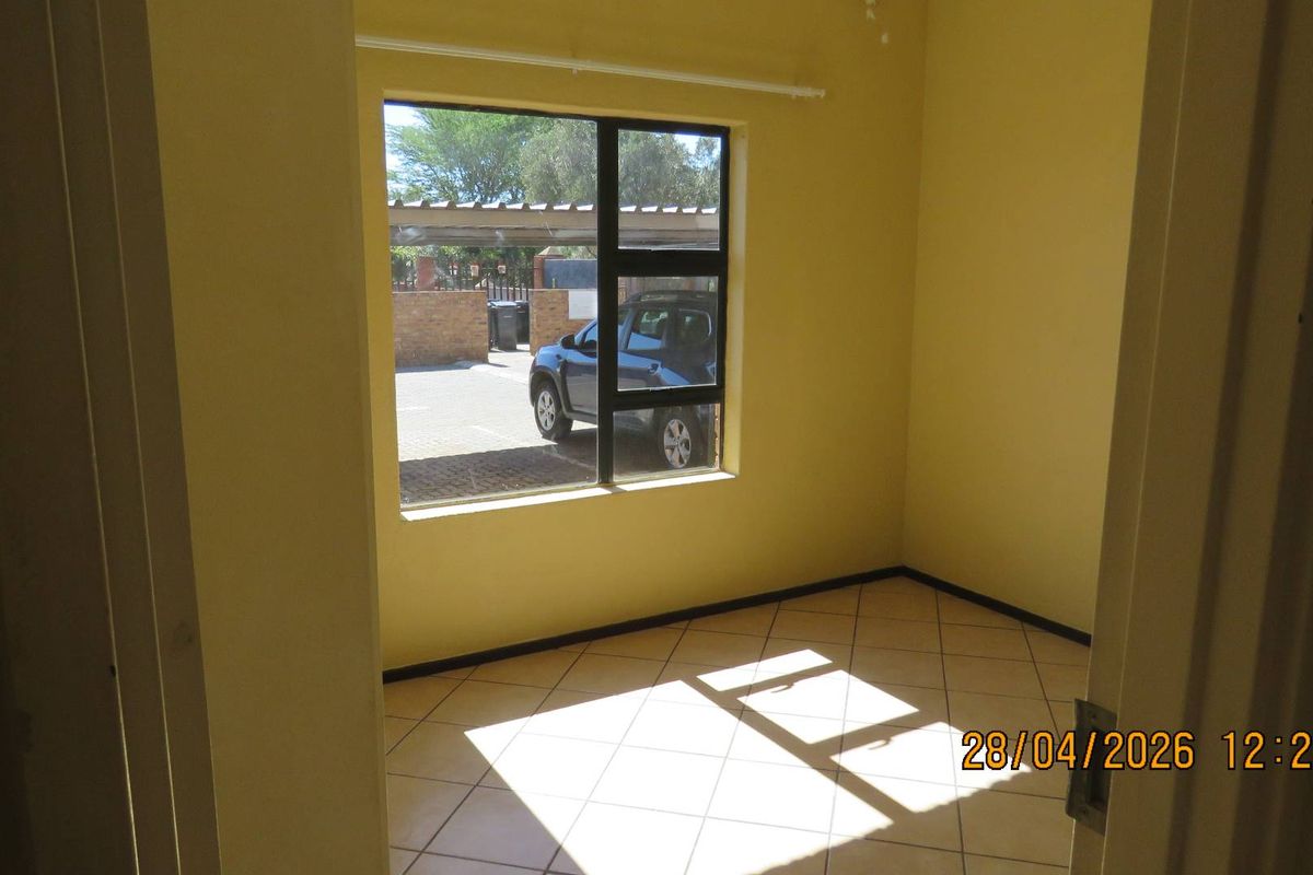 A vacant bedroom featuring tiled flooring and a large window providing natural light and a view of the exterior parking area.