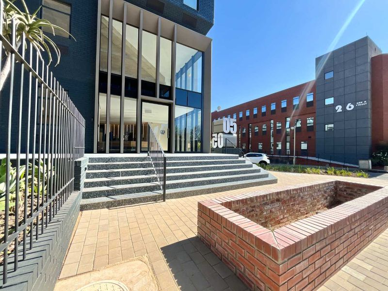 Modern office building entrance featuring a glass facade, terrazzo steps, and a brick planter box in a well-maintained urban setting.