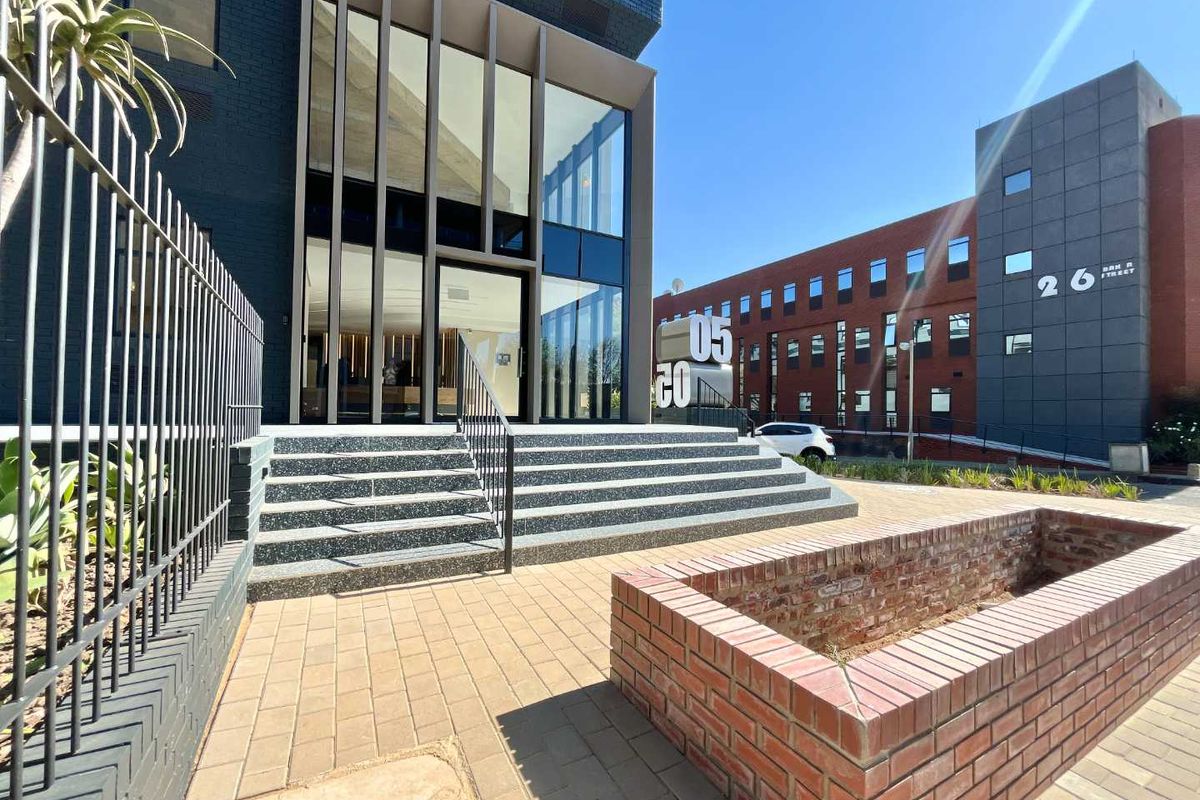 Modern office building entrance featuring a glass facade, terrazzo steps, and a brick planter box in a well-maintained urban setting.