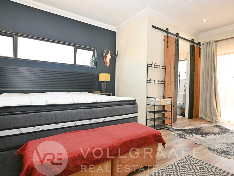 A well-maintained bedroom featuring modern sliding barn doors leading to an en-suite, laminate flooring, and a large horizontal window for natural light.