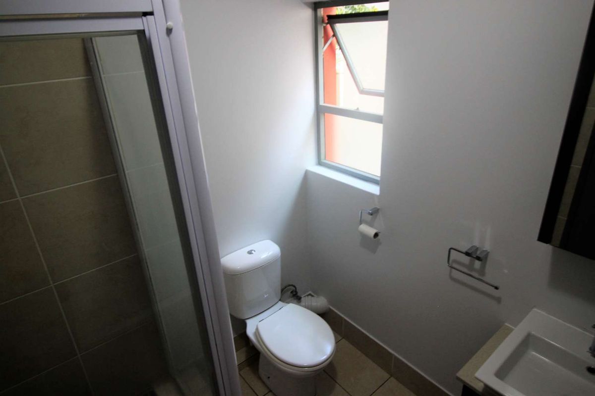 A functional bathroom featuring a shower enclosure, a standard toilet, and a wall-mounted basin with tiled flooring and a window for natural ventilation.