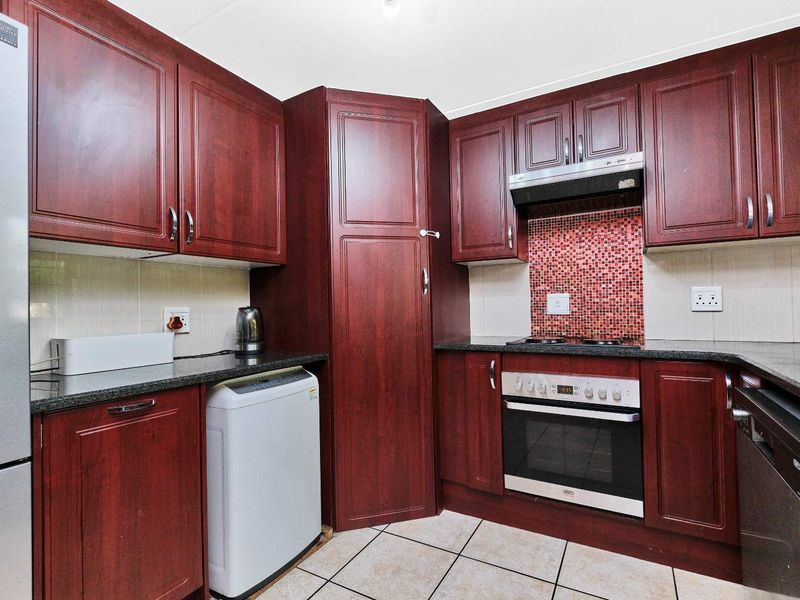 A functional kitchen featuring dark wood cabinetry, granite countertops, a built-in oven, hob, extractor fan, and tiled backsplash.