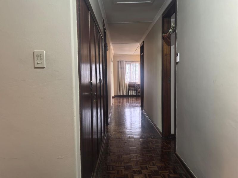 A long hallway featuring traditional parquet flooring and wooden door frames, leading towards a naturally lit area at the end of the corridor.