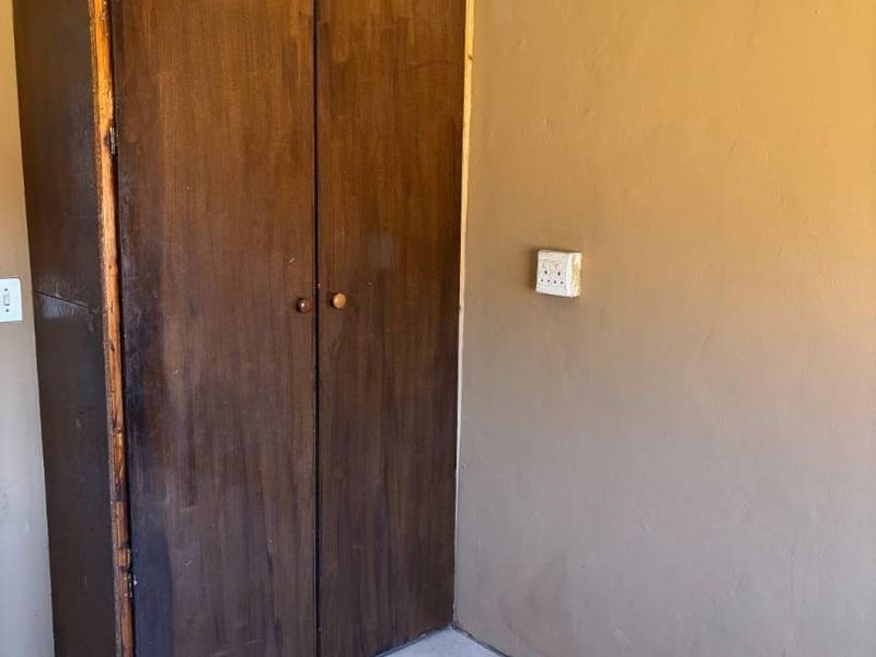 A simple bedroom space featuring tiled flooring and a built-in wooden cupboard, offering a blank canvas for potential updates.