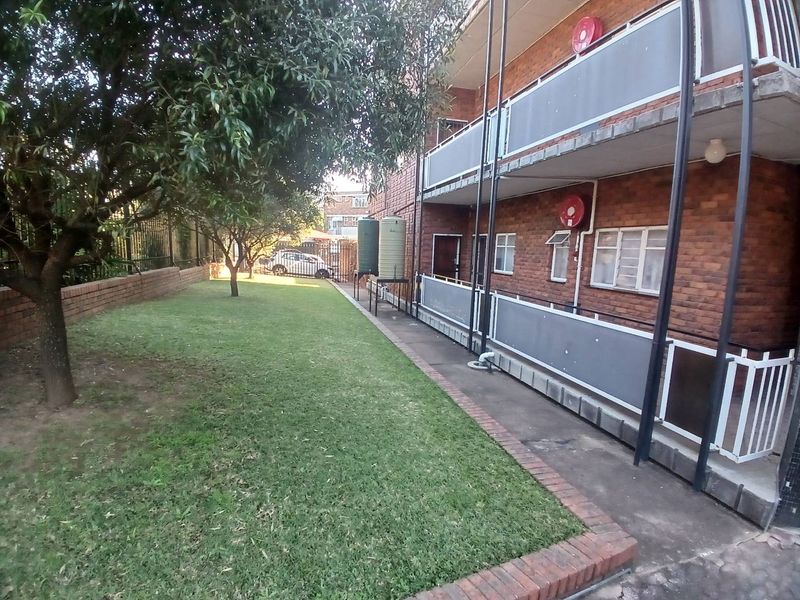 Rear view of the apartment building featuring a communal lawn, paved walkway, and multi-level balconies with brick exterior finishes.