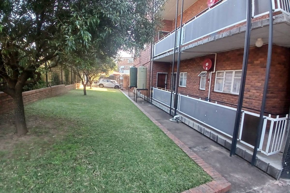 Rear view of the apartment building featuring a communal lawn, paved walkway, and multi-level balconies with brick exterior finishes.