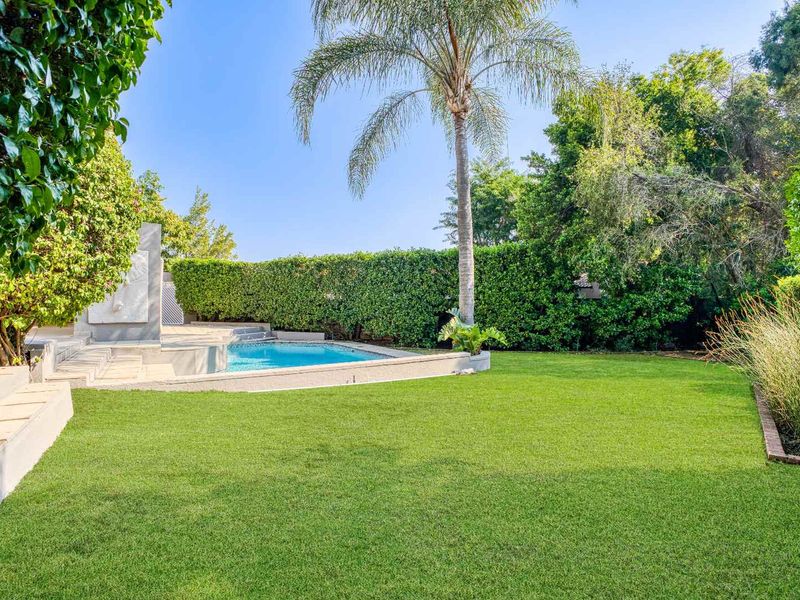 A well-maintained backyard featuring a swimming pool, lush green lawn, and mature garden hedging providing privacy.