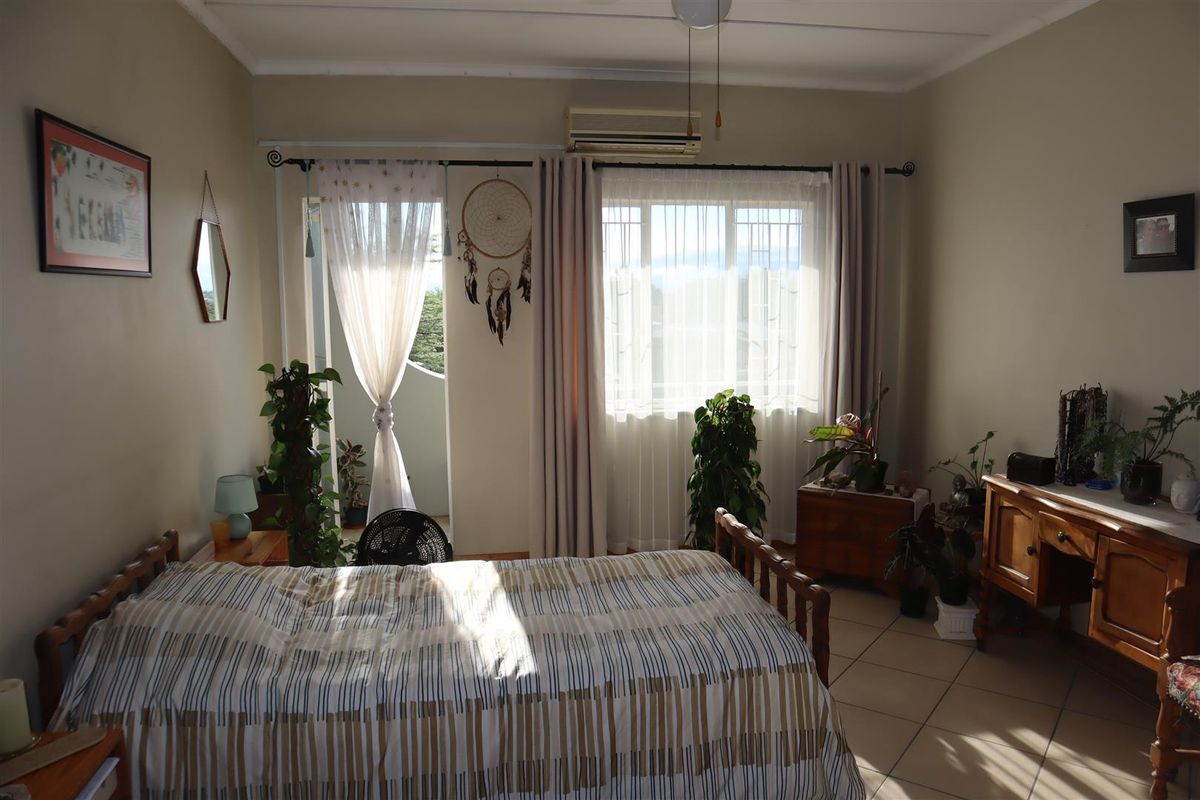 A bedroom featuring tiled flooring, a wall-mounted air conditioning unit, and direct access to a private balcony through a glass door.