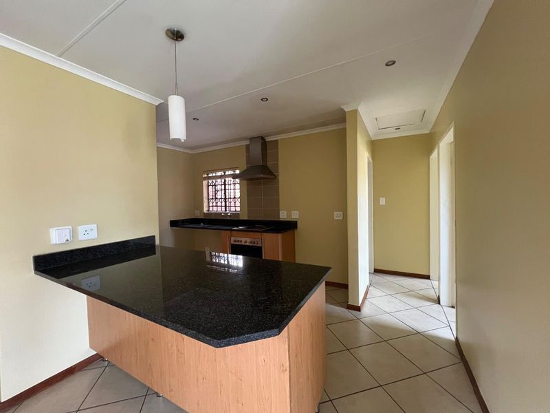 An open-plan kitchen featuring granite countertops, a breakfast bar, built-in oven, and extractor fan, with tiled flooring throughout.