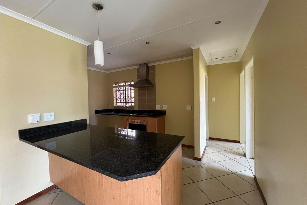 An open-plan kitchen featuring granite countertops, a breakfast bar, built-in oven, and extractor fan, with tiled flooring throughout.