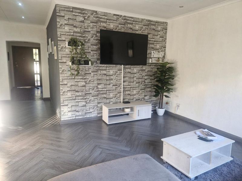 A modern living room featuring a striking stone-effect feature wall, herringbone-patterned flooring, and recessed ceiling lighting.
