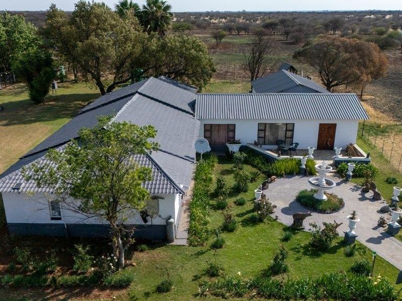 Aerial view of a farm property featuring a main dwelling with a tiled roof, a paved courtyard with a fountain, and established garden grounds.