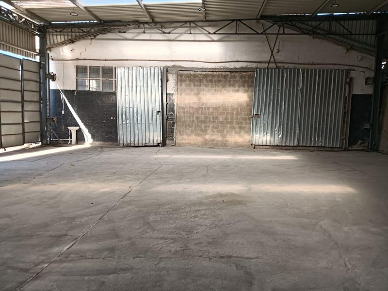 Spacious industrial utility area featuring concrete flooring, exposed steel roof trusses, and large corrugated metal sliding doors.
