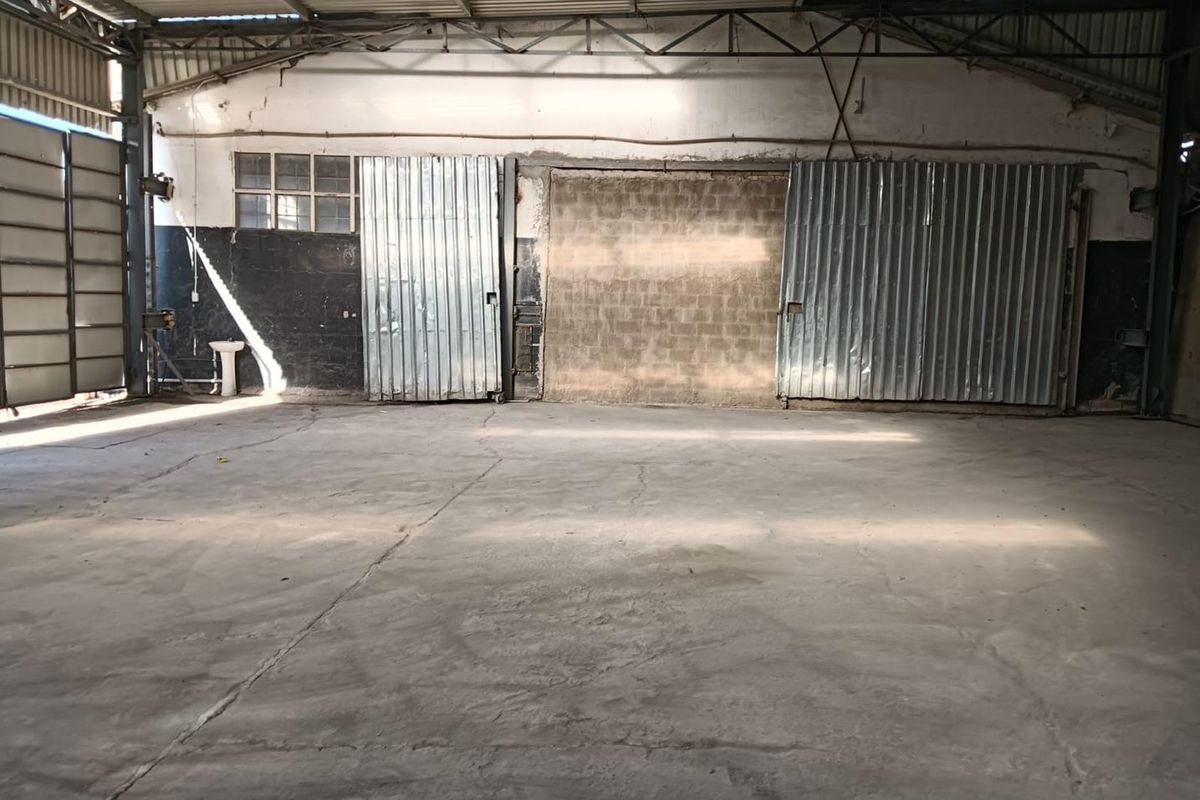 Spacious industrial utility area featuring concrete flooring, exposed steel roof trusses, and large corrugated metal sliding doors.