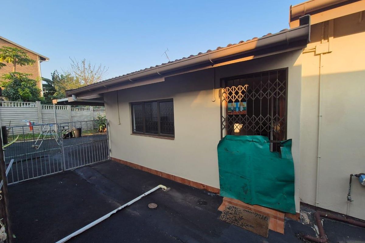 Rear exterior view of the property featuring a paved area, security gate, and basic building structure with guttering and boundary wall.