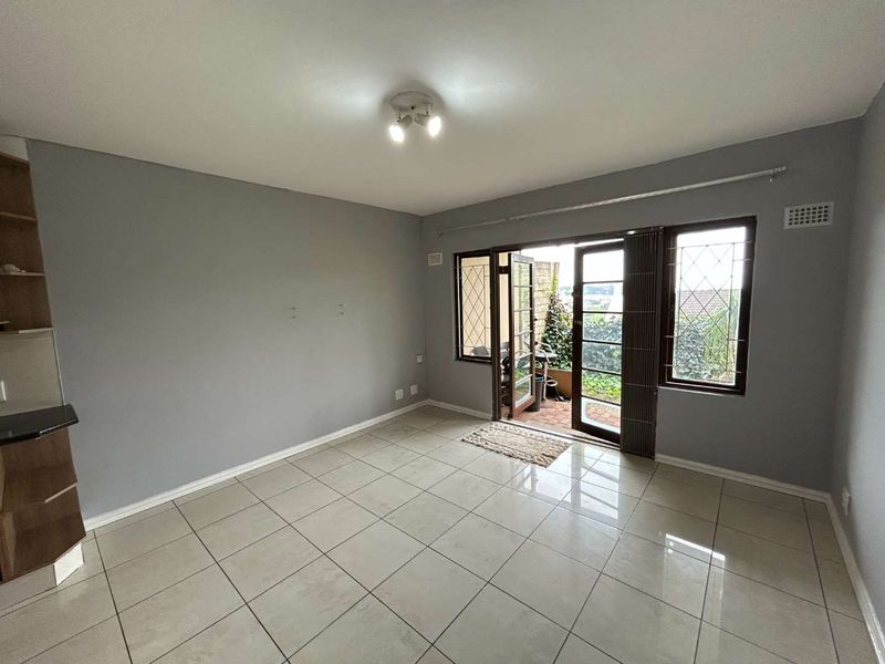 An empty living room featuring neutral tiled flooring, grey walls, and french doors leading to an outdoor patio area.
