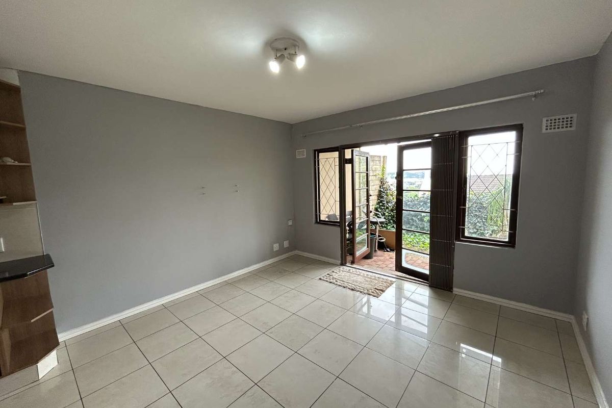 An empty living room featuring neutral tiled flooring, grey walls, and french doors leading to an outdoor patio area.