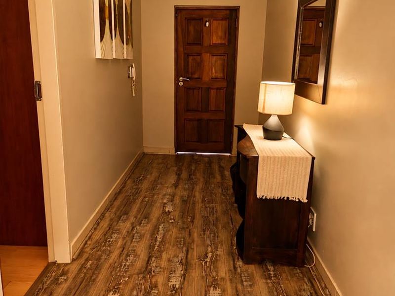 A well-maintained hallway featuring wood-look laminate flooring, crown molding, and a solid timber door, creating a warm and inviting entrance.