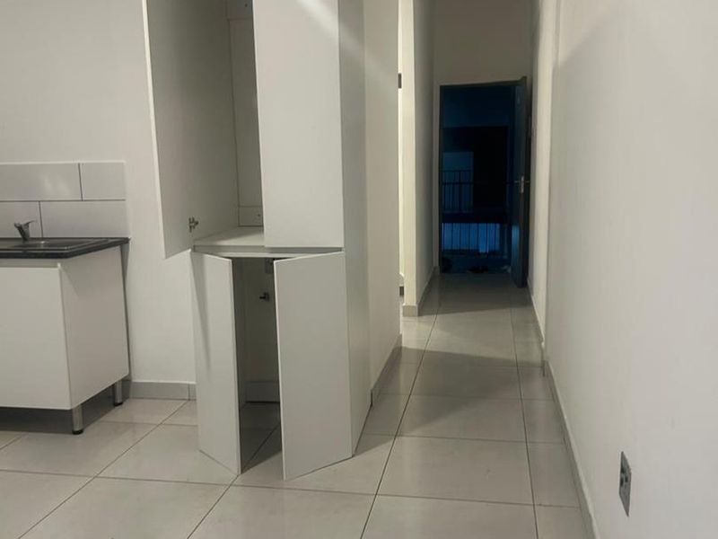 A compact kitchen area featuring white cabinetry, a sink, and tiled flooring, leading into a hallway.