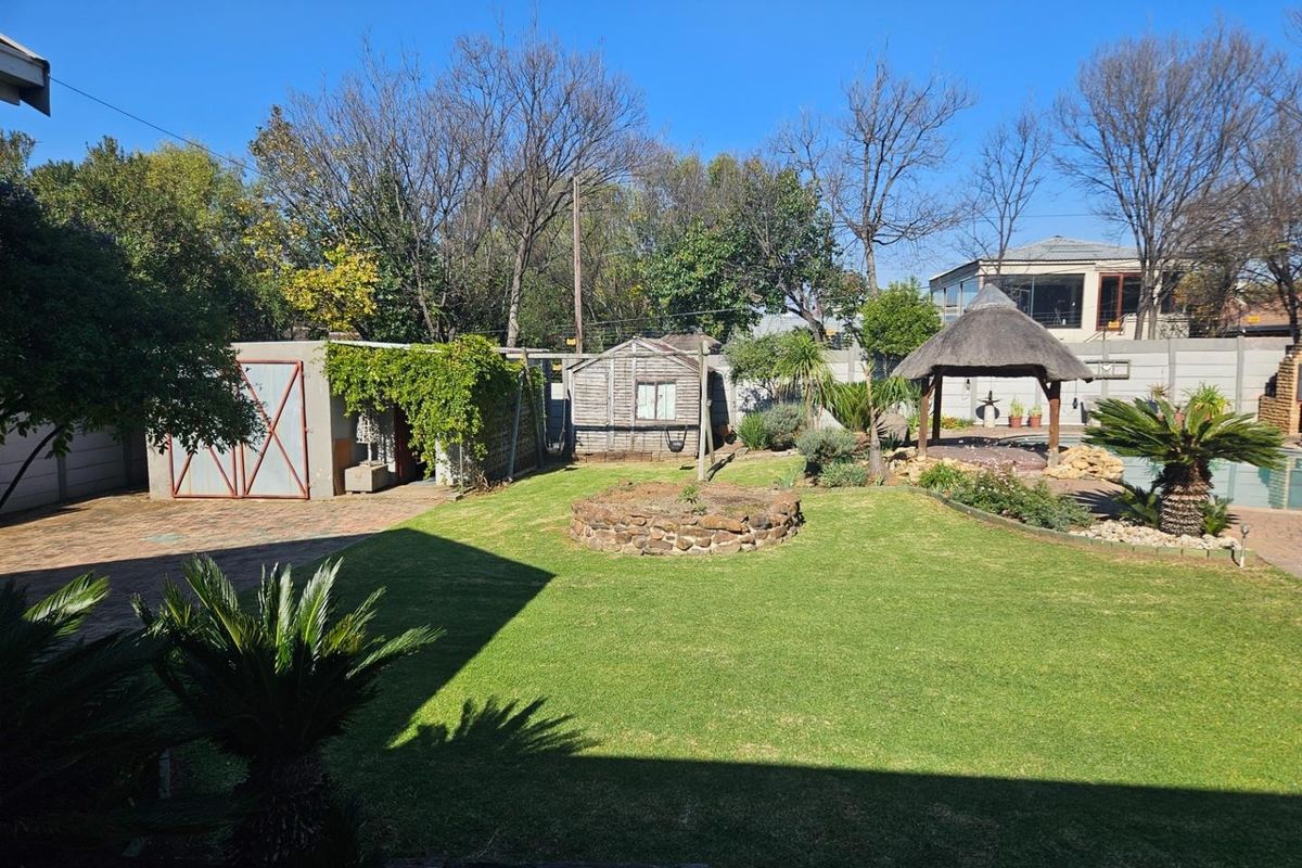 A spacious rear garden featuring a manicured lawn, a thatched gazebo, a stone fire pit area, and a detached storage shed.