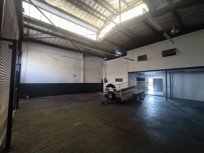 Spacious industrial warehouse unit featuring high ceilings with skylights, concrete flooring, a mezzanine level, and a large roller door for easy access.