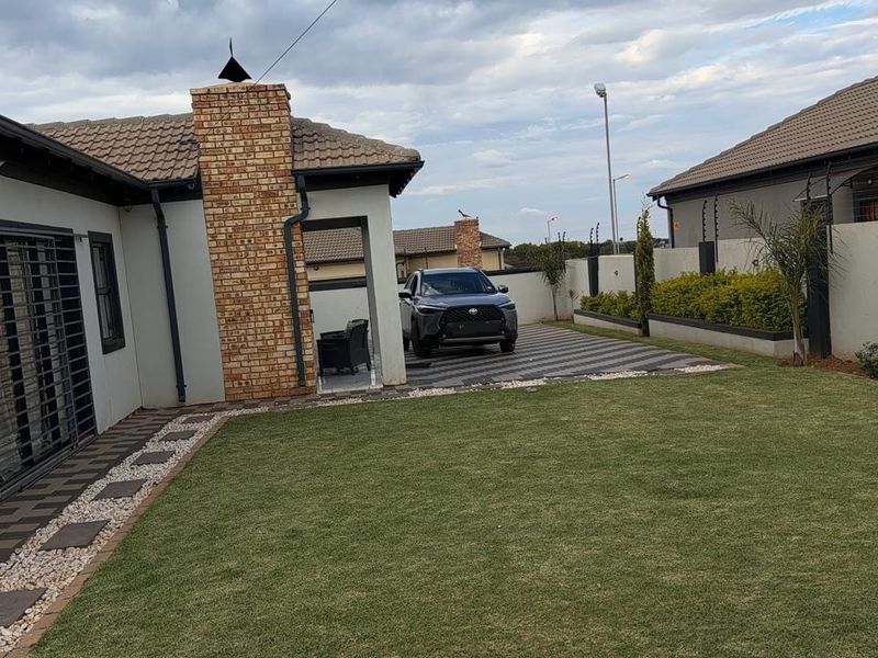 A well-maintained rear exterior featuring a brick chimney, paved driveway, and a neat lawn enclosed by boundary walls with electric fencing.
